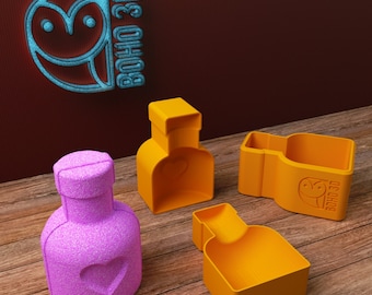 May include: Three orange plastic molds for making chocolate in the shape of bottles with heart-shaped details. The molds are on a wooden surface. The text "BOHO 3D" is visible on one of the molds.
