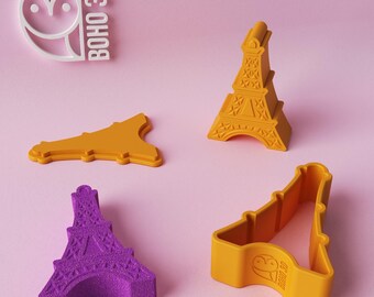 May include: Four Eiffel Tower cookie cutters, two are yellow and two are purple. The yellow cutters are made by BOHO 3D. The purple cutter is made by BOHO 3D.