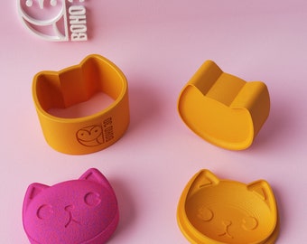 May include: Four cat-shaped 3D-printed objects in orange and pink, including a ring, a bowl, and two cat face molds. The Boho 3D logo is visible in white and orange. The objects are on a pink background.