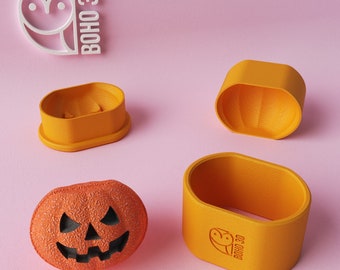 May include: A set of four orange plastic pumpkin-shaped molds with the text "BOHO 3D" on one of the molds. The molds are on a pink surface.