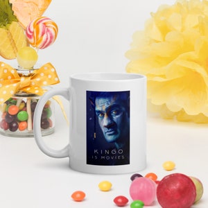Peut inclure: Une tasse à café en céramique blanche avec une image bleue et noire d'un homme avec le texte "KINGO IS MOVIES" imprimé sur le devant.