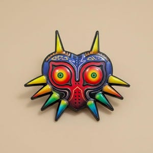 May include: A colorful, heart-shaped mask with a detailed design. The mask features a red center, blue and yellow accents, and green eyes. The mask has sharp, pointed edges and is likely a decorative item.