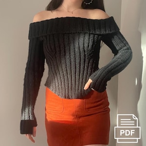 Könnte beinhalten: Schwarzer Off-Shoulder-Pullover mit gerippter Strickstruktur. Der Pullover hat lange Ärmel und eine verkürzte Länge.