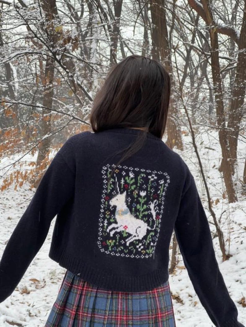 Peut inclure: Un cardigan bleu marine court avec une licorne blanche brod&eacute;e au dos. Le cardigan est en tricot torsad&eacute; et se ferme par des boutons.