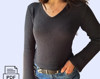 May include: Black long-sleeved sweater with a v-neck and a ribbed texture. The sweater is cropped and is being worn with blue jeans.