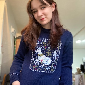 May include: A navy blue knitted sweater with a white unicorn and floral design.