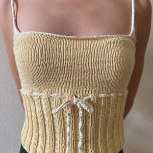 K&ouml;nnte beinhalten: Ein gelbes Stricktop mit wei&szlig;en R&auml;ndern und einer wei&szlig;en Schleife an der Taille.