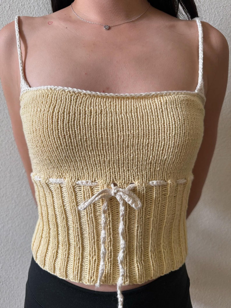K&ouml;nnte beinhalten: Ein gelbes Stricktop mit wei&szlig;en R&auml;ndern und einer wei&szlig;en Schleife an der Taille.