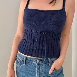 K&ouml;nnte beinhalten: Ein marineblaues Stricktop mit einem Band in der Taille. Das Top ist &auml;rmellos und hat einen quadratischen Ausschnitt.