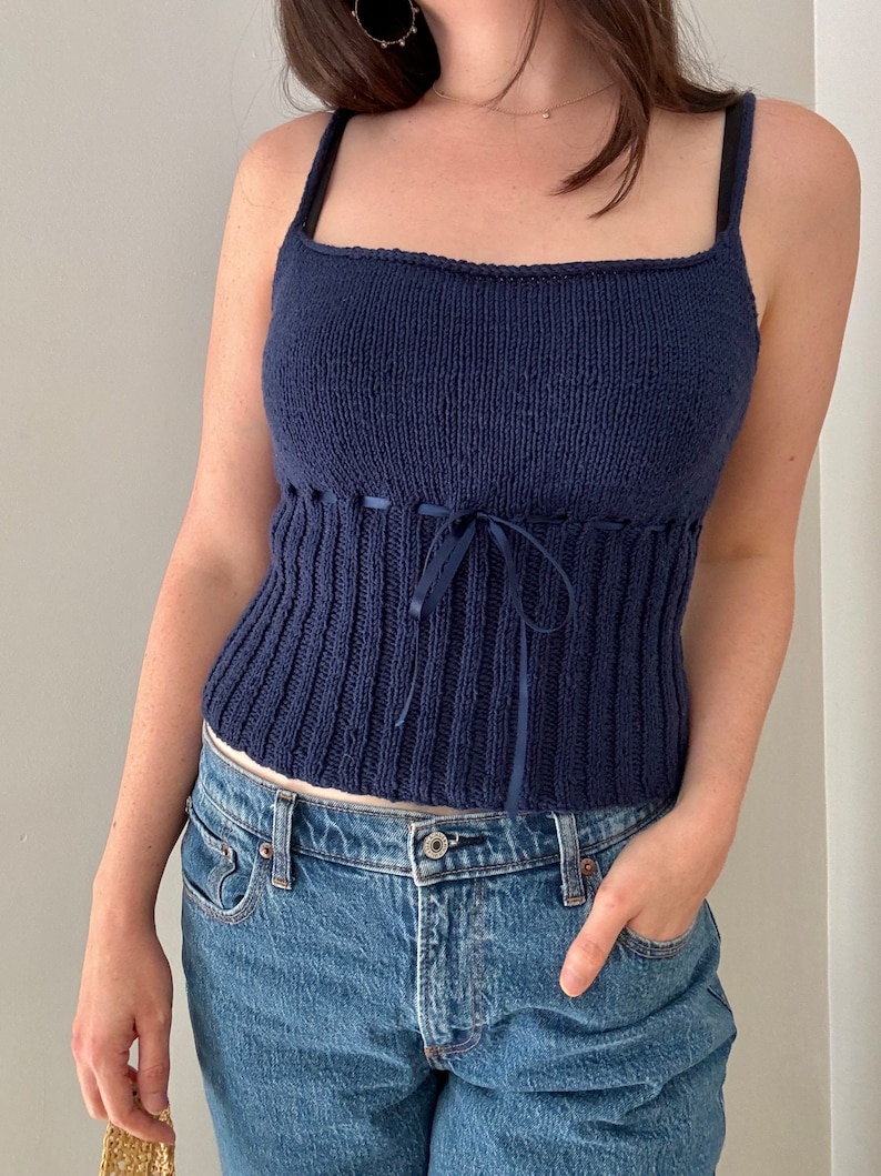 K&ouml;nnte beinhalten: Ein marineblaues Stricktop mit einem Band in der Taille. Das Top ist &auml;rmellos und hat einen quadratischen Ausschnitt.