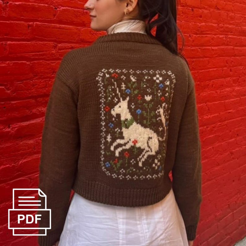 Peut inclure: Un cardigan court marron avec une broderie de licorne blanche sur le dos. La licorne est entour&eacute;e de fleurs et de feuilles dans des tons de vert, bleu et rouge.