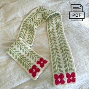 May include: Cream-colored knitted scarf with a green leaf pattern and red flower accents. The scarf is made of soft yarn and has a PDF icon in the upper right corner.