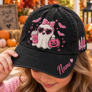 May include: A black denim baseball cap featuring an embroidered white ghost wearing pink heart-shaped sunglasses and a pink polka-dot bow. The ghost holds a pink drink and a pumpkin bucket, surrounded by pink bats, stars, and the word Name.