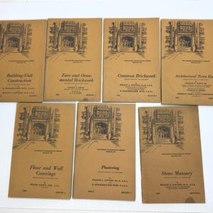 May include: A collection of vintage architectural textbooks with tan covers. Each book features a detailed illustration of a building's facade and titles such as "Building-Unit Construction" and "Common Brickwork". The books are from the International Correspondence Schools.