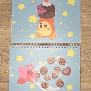 May include: Two spiral bound notebooks with a blue background and white stars. The top notebook features a pink and orange cartoon character holding a chocolate cake with a cherry on top. The bottom notebook features a pink cartoon character with a wide open mouth blowing a stream of chocolate hearts and squares.