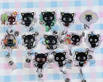 May include: A collection of twelve retractable badge reels featuring black cat characters with glittery details. Each reel displays a unique scene, including cats with accessories like glasses, party hats, or sports items, attached to clear plastic clips.