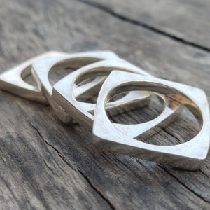May include: Four silver square-shaped rings stacked on top of each other on a wooden surface.