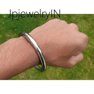 Puede incluir: Un brazalete de plata en la muñeca de una persona. El brazalete es simple y redondo.