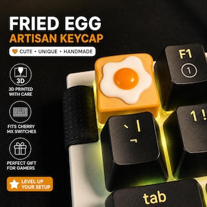 May include: A custom artisan keycap in the shape of a fried egg, with a yellow yolk and white egg white, is on a keyboard. The keycap is 3D printed and fits Cherry MX switches. The text "FRIED EGG ARTISAN KEYCAP" is at the top.