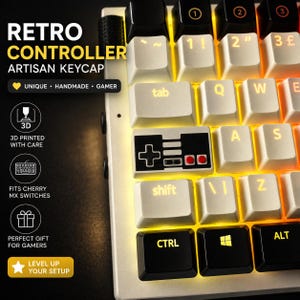 May include: Close-up of a retro-style keyboard with white keycaps and yellow backlighting. The keyboard features a black controller keycap and the text "RETRO CONTROLLER ARTISAN KEYCAP". The keyboard is designed for gamers.