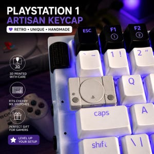 Könnte beinhalten: Eine weiße Tastatur mit einer individuellen Artisan-Tastenkappe in Form einer PlayStation 1-Konsole. Die Tastenkappe ist grau mit schwarzen Tasten und einem PlayStation-Logo. Die Tastatur hat auch weiße und schwarze Tasten mit blauer Hintergrundbeleuchtung. Der Text auf dem Bild lautet "PLAYSTATION 1 ARTISAN KEYCAP".