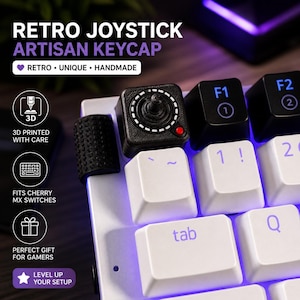May include: A black retro joystick artisan keycap with a red button, installed on a white keyboard. The keycap is next to other black and white keys. Text on the image reads "Retro Joystick Artisan Keycap".