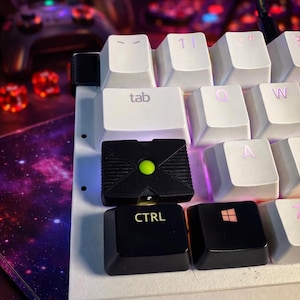 May include: Close-up of a mechanical keyboard with white keycaps and black accent keys. The black keycaps include the "CTRL" key and a key with the Windows logo. A custom keycap with a green center button and an Xbox logo is also visible.