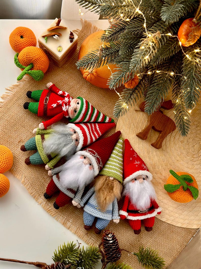May include: Five crocheted gnomes with different colored hats and outfits. The gnomes are arranged in a semi-circle on a brown burlap surface. The gnomes are wearing red, green, blue, and white hats and outfits.
