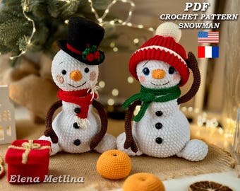 May include: Two crocheted snowman amigurumi toys. One snowman wears a red and white hat and a green scarf. The other snowman wears a black top hat and a red scarf. Both snowmen have black eyes and buttons. The snowmen are sitting on a brown burlap surface.