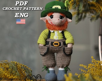 Könnte beinhalten: Gehäkelte Koboldpuppe mit grünem Hut mit Kleeblatt, grünem Hemd, brauner Latzhose und blauen Schuhen. Die Puppe hat einen roten Bart und hält ein kleines grünes Kleeblatt. Der Text "PDF CROCHET PATTERN ENG" befindet sich oben links.