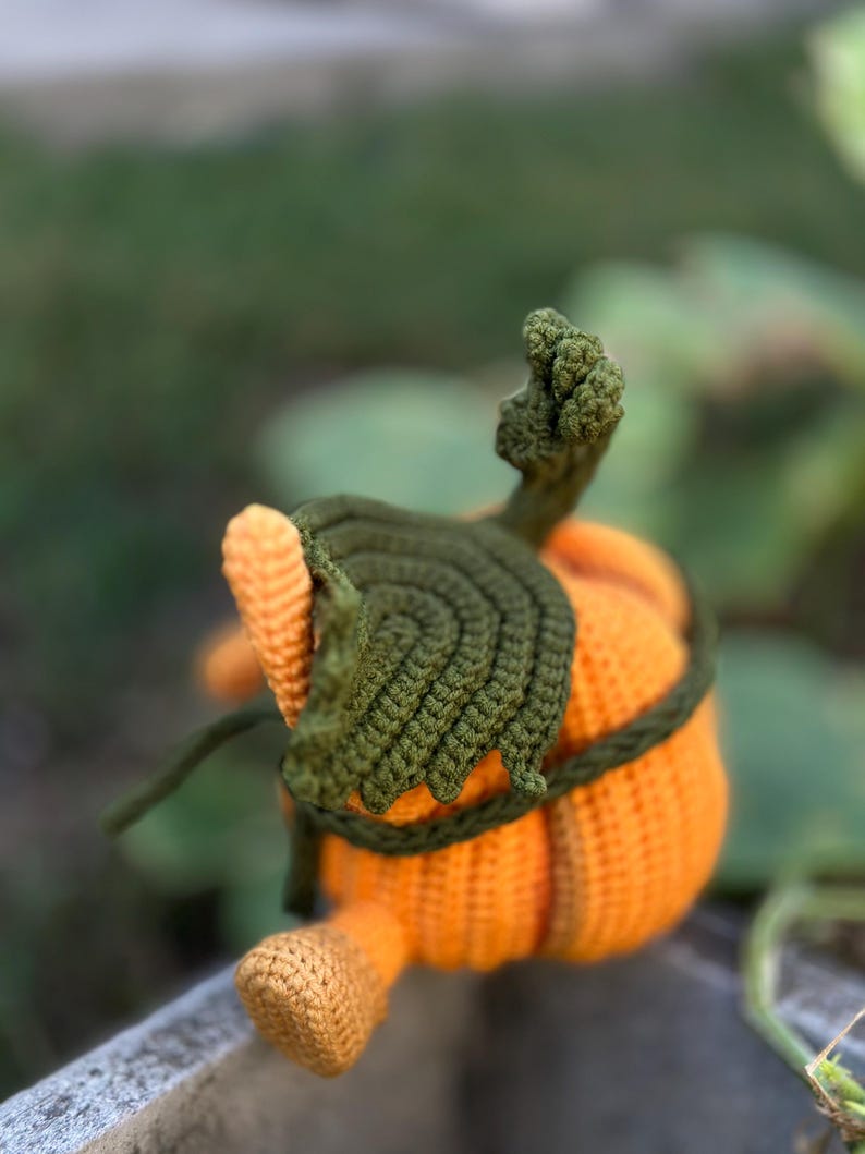 May include: A crocheted pumpkin toy with a green stem and leaves. The pumpkin is orange and has a textured surface.