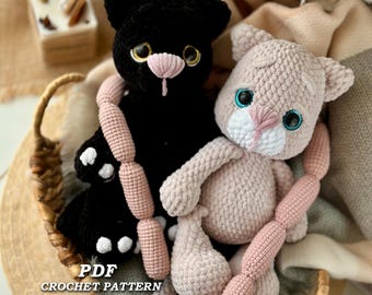 May include: Two crocheted cat plushies, one black and one light pink, sit in a woven basket. The black cat has yellow eyes and white paw pads. The pink cat has blue eyes. Both have pink sausage-shaped accessories. Text reads "PDF CROCHET PATTERN PIUSH KITTY Eng."