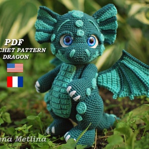 以下が含まれることがあります： ターコイズグリーンのドラゴンアミグルミのおもちゃのPDF編み図。ドラゴンは大きな青い目と白い爪をしています。このパターンは英語とフランス語で入手できます。