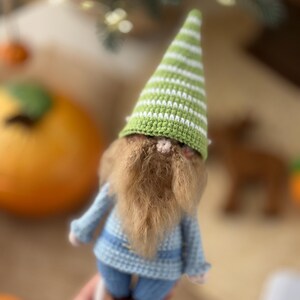 May include: A crocheted gnome doll with a green and white striped hat, a brown beard, and a blue knitted outfit.