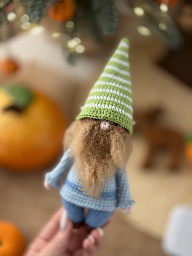 May include: A crocheted gnome doll with a green and white striped hat, a brown beard, and a blue knitted outfit.