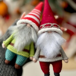 May include: Two crocheted gnomes, one with a red and white striped hat and green pants, the other with a solid red hat and red pants.