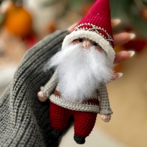 May include: A crocheted gnome ornament with a red hat, white beard, and gray and red clothing.