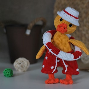 May include: A crocheted yellow duck wearing a red and white life preserver, red and white polka dot swim trunks, and a white and red striped hat.