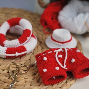 May include: A crocheted red and white swimsuit with white polka dots, a white crocheted hat with a red band, and a red and white crocheted life preserver.