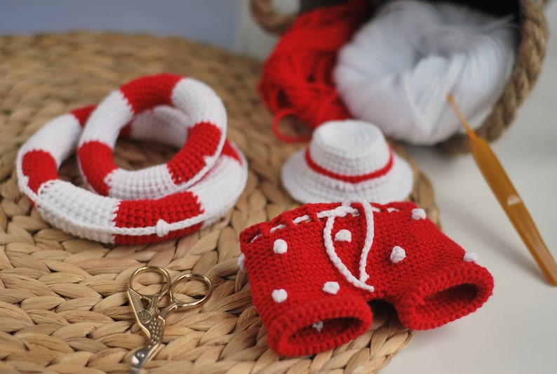 May include: A crocheted red and white swimsuit with white polka dots, a white crocheted hat with a red band, and a red and white crocheted life preserver.