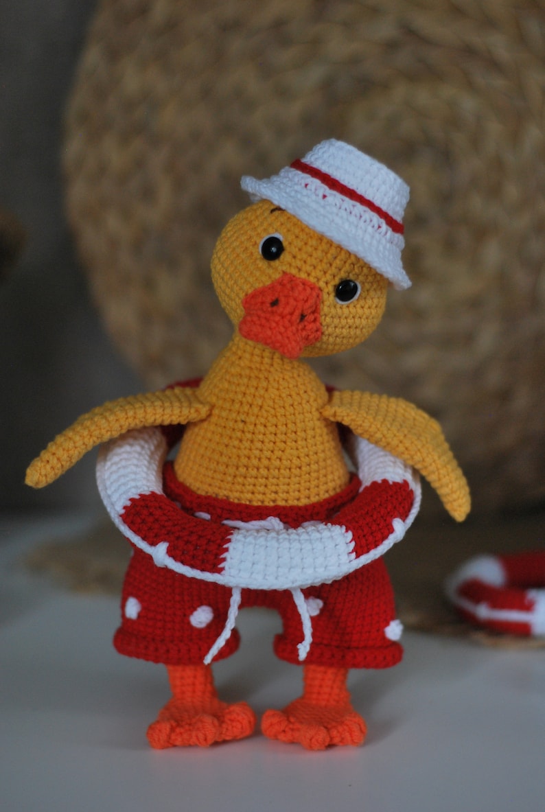 May include: A crocheted yellow duck wearing a white hat with a red stripe, red and white polka dot shorts, and a red and white life preserver.