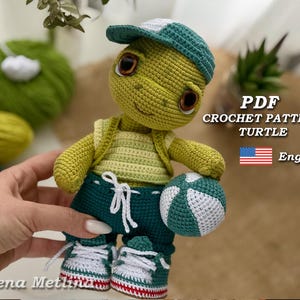Può includere: Una bambola di tartaruga all'uncinetto con un berretto da baseball verde e bianco, un gilet giallo e pantaloncini verde scuro. La tartaruga tiene in mano una palla verde e bianca. Il testo "PDF CROCHET PATTERN TURTLE Eng" è visibile.