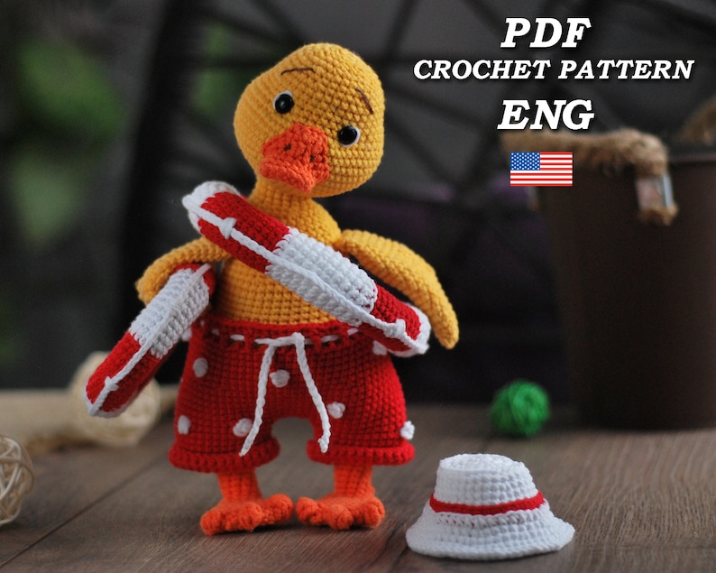 May include: A crocheted yellow duck wearing red and white swim trunks and a red and white life preserver. The duck is holding the life preserver in its right wing. The duck is sitting on a wooden surface.  PDF CROCHET PATTERN ENG