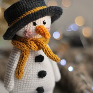 May include: A crocheted snowman toy with a black hat, yellow scarf, and black buttons. The snowman is wearing blue boots with white pom-poms.