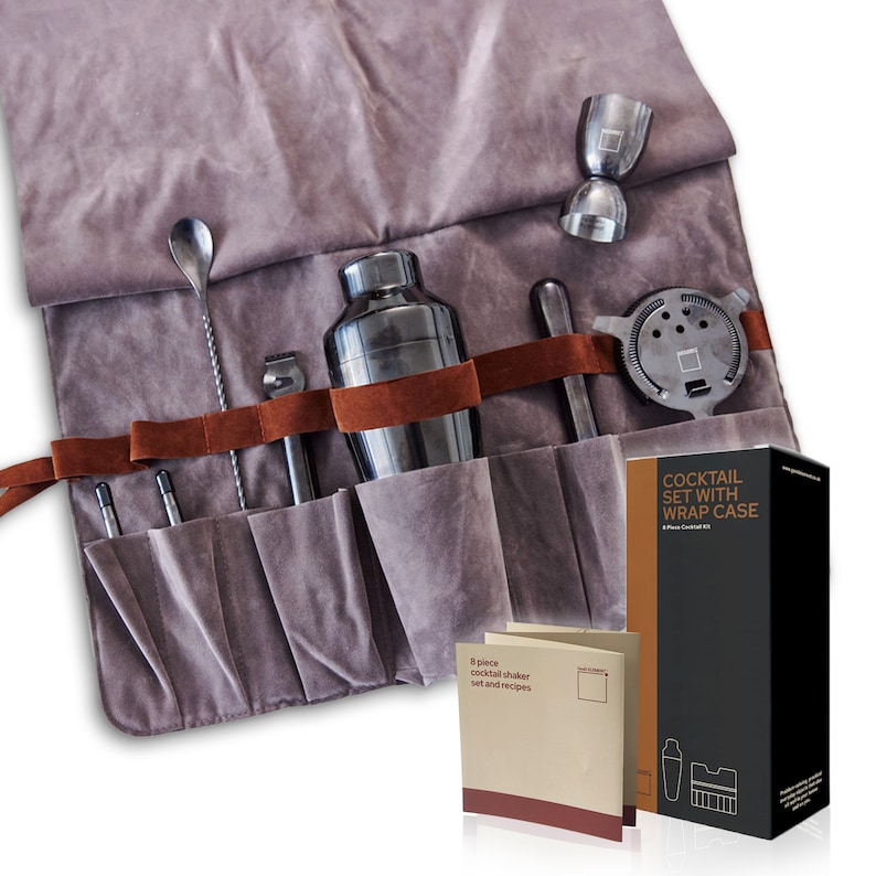 May include: A gray velvet roll-up case with brown leather straps holds a cocktail shaker set. The set includes a cocktail shaker, a jigger, a muddler, a bar spoon, a strainer, and two mixing sticks. The case also includes a small booklet with cocktail recipes. The case has the text "Cocktail Set with Wrap Case" printed on the side.