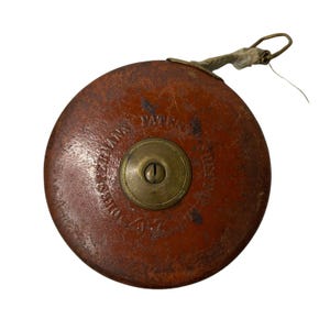 May include: A vintage brown leather measuring tape with a brass center and a fabric loop. The tape measure has the text "JOHN STEVENS PATENT" around the brass center. The leather casing shows signs of wear.