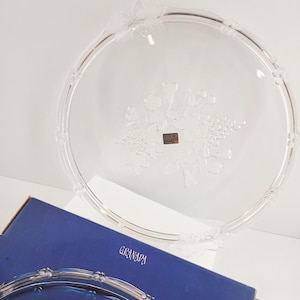 May include: A clear glass serving platter with a floral design in the center. The platter has a decorative rim and is partially visible with a blue box that reads "GRANADA".