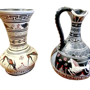 Könnte beinhalten: Zwei Keramikvasen mit schwarzen und weißen geometrischen Mustern und roten Akzenten. Eine Vase ist eine hohe, schlanke Vase mit einem schmalen Hals und einer breiten Basis. Die andere Vase ist eine kürzere, rundere Vase mit einem Henkel. Beide Vasen zeigen stilisierte Tierfiguren.