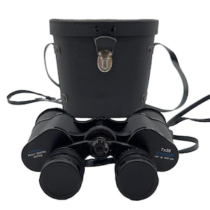May include: Black binoculars with a matching black leather case. The binoculars have the text "7x35 ENSIGN" and "FULLY COATED OPTICS". The case has a handle and a clasp closure. The binoculars are designed for viewing at 394 feet at 1000 yards.