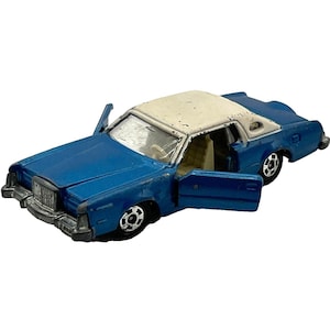 May include: A blue and white toy car with the doors open. The car has a white roof and a blue body. The car has black wheels and a silver grill. The car is a vintage model.